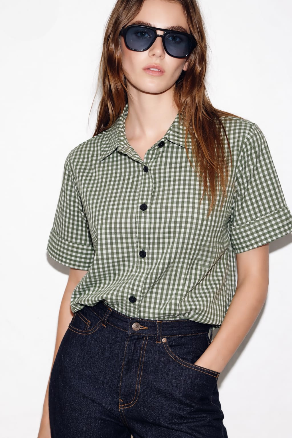 Person wearing a green checkered shirt and sunglasses on a white background