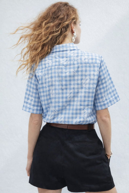 Person wearing a blue and white checkered shirt and black shorts against a light gray background