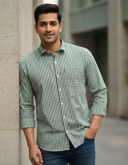Man wearing a green checkered shirt leaning against a wall.