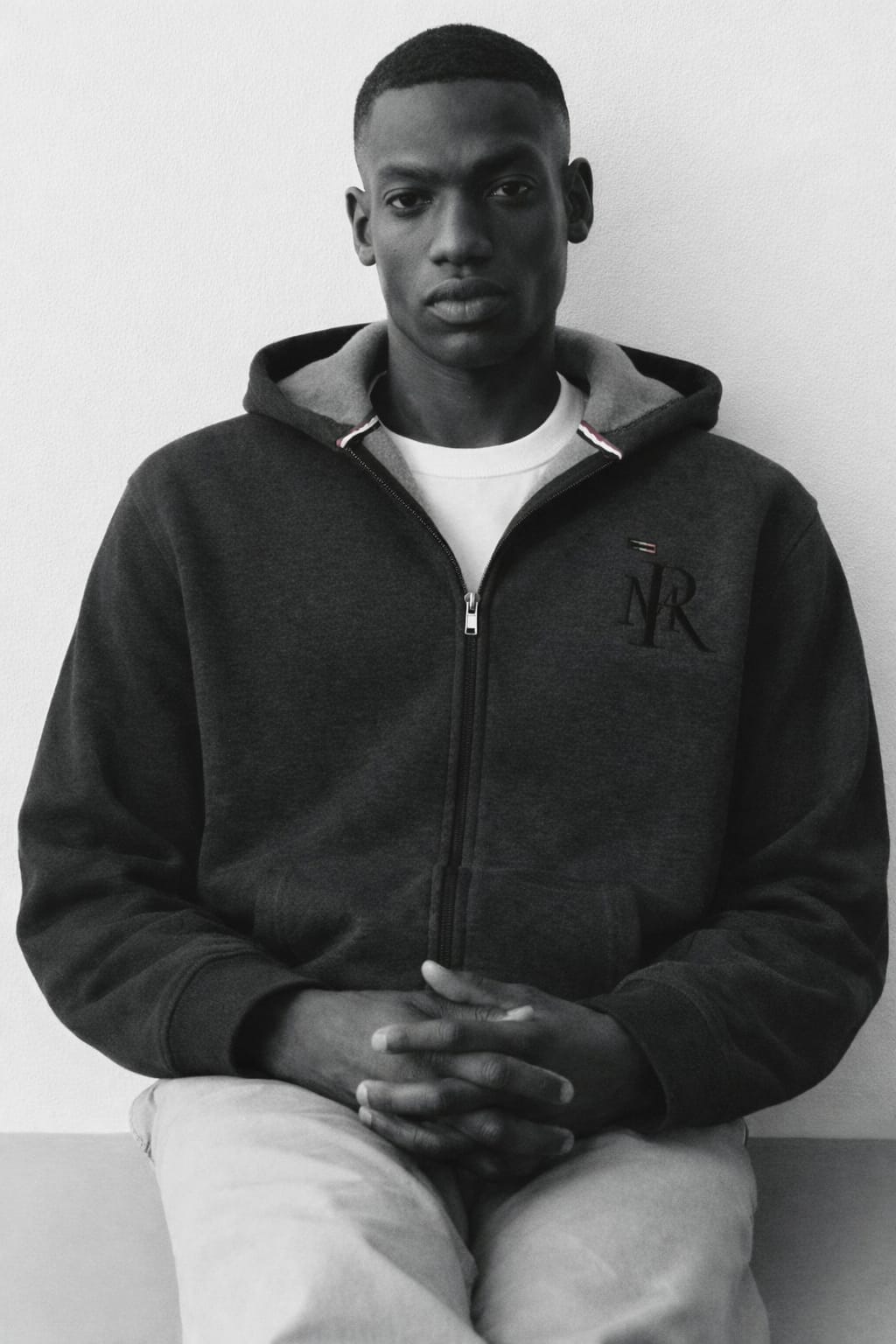 Person wearing a dark hoodie with a logo, sitting against a plain background