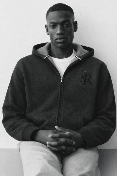 Person wearing a dark hoodie with a logo, sitting against a plain background