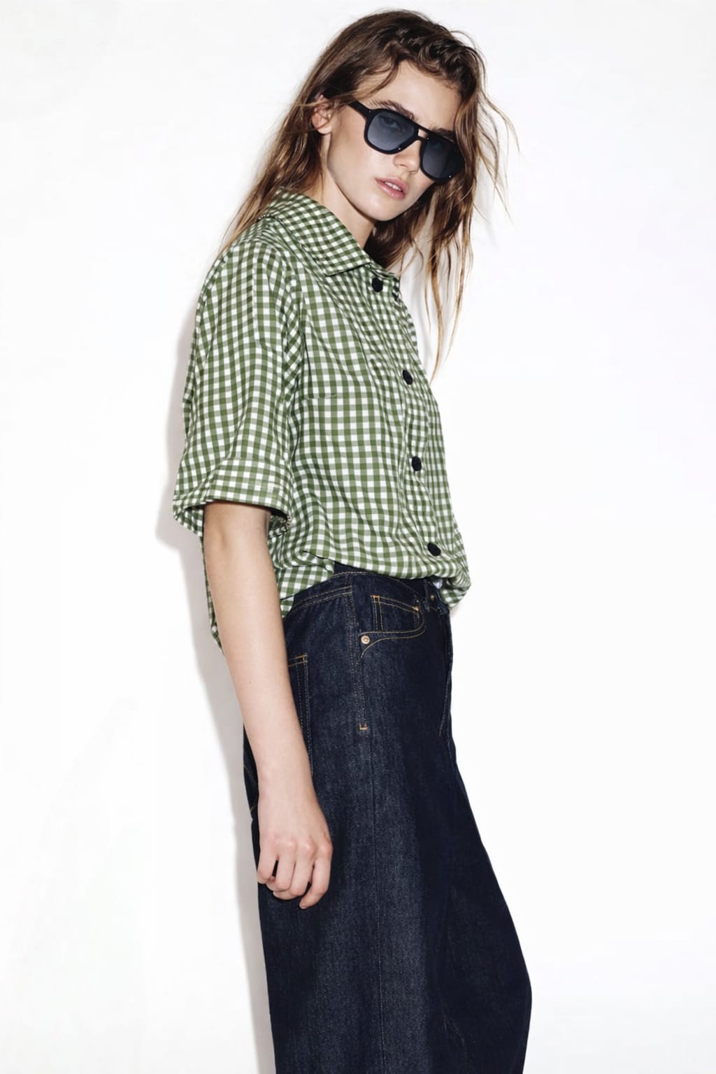 Person wearing a green checkered shirt and dark jeans on a white background