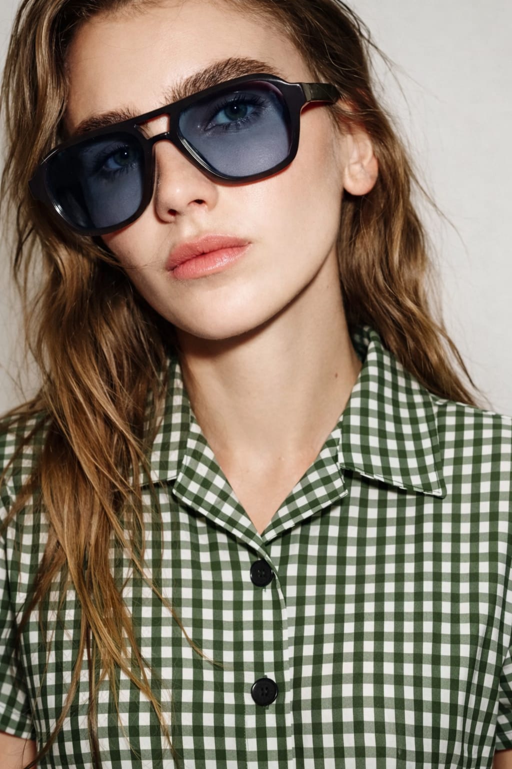 Person wearing sunglasses and a green checkered shirt against a neutral background