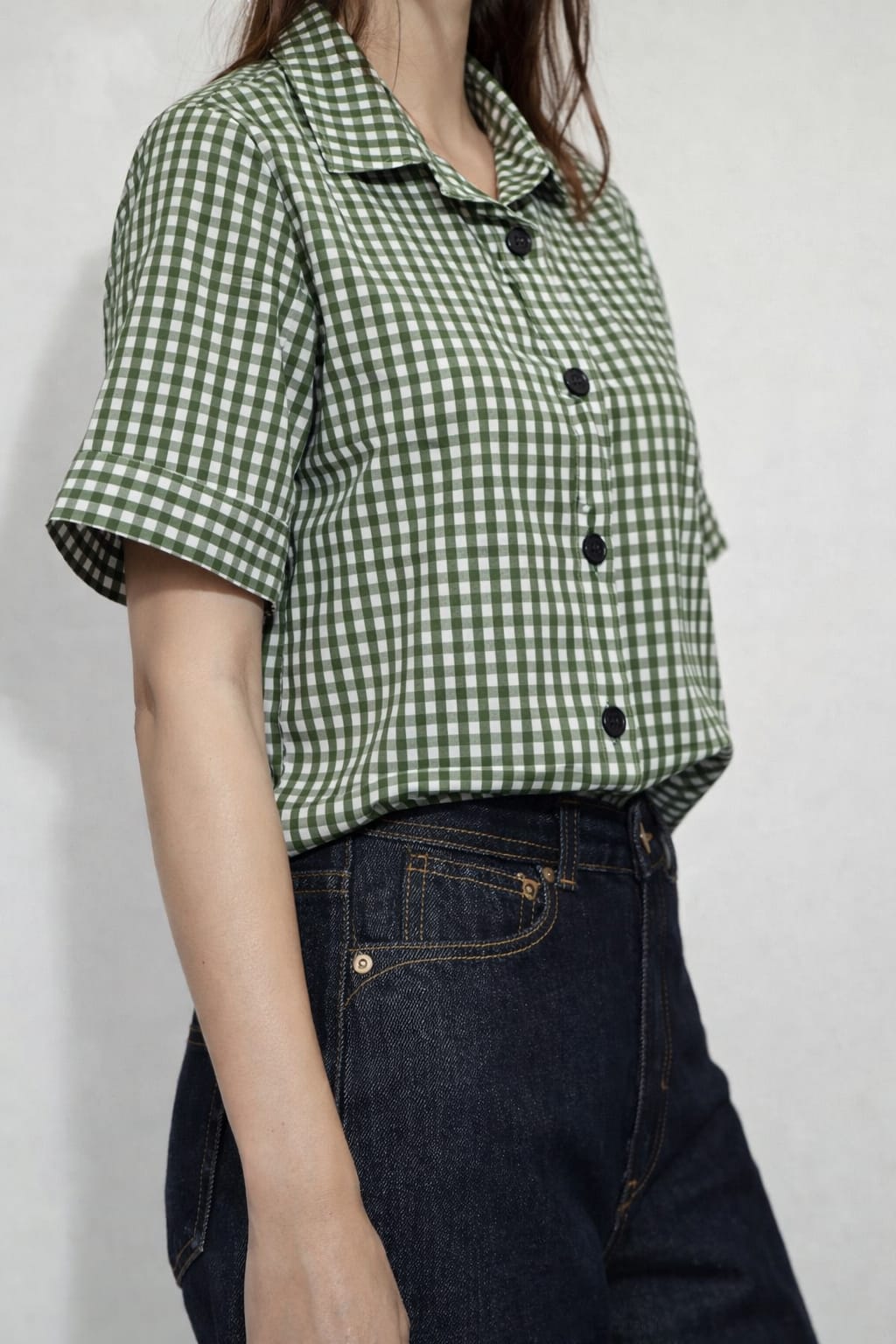 Person wearing a green checkered shirt and dark jeans against a plain background