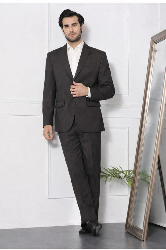 Man wearing a dark suit standing next to a mirror against a white wall.