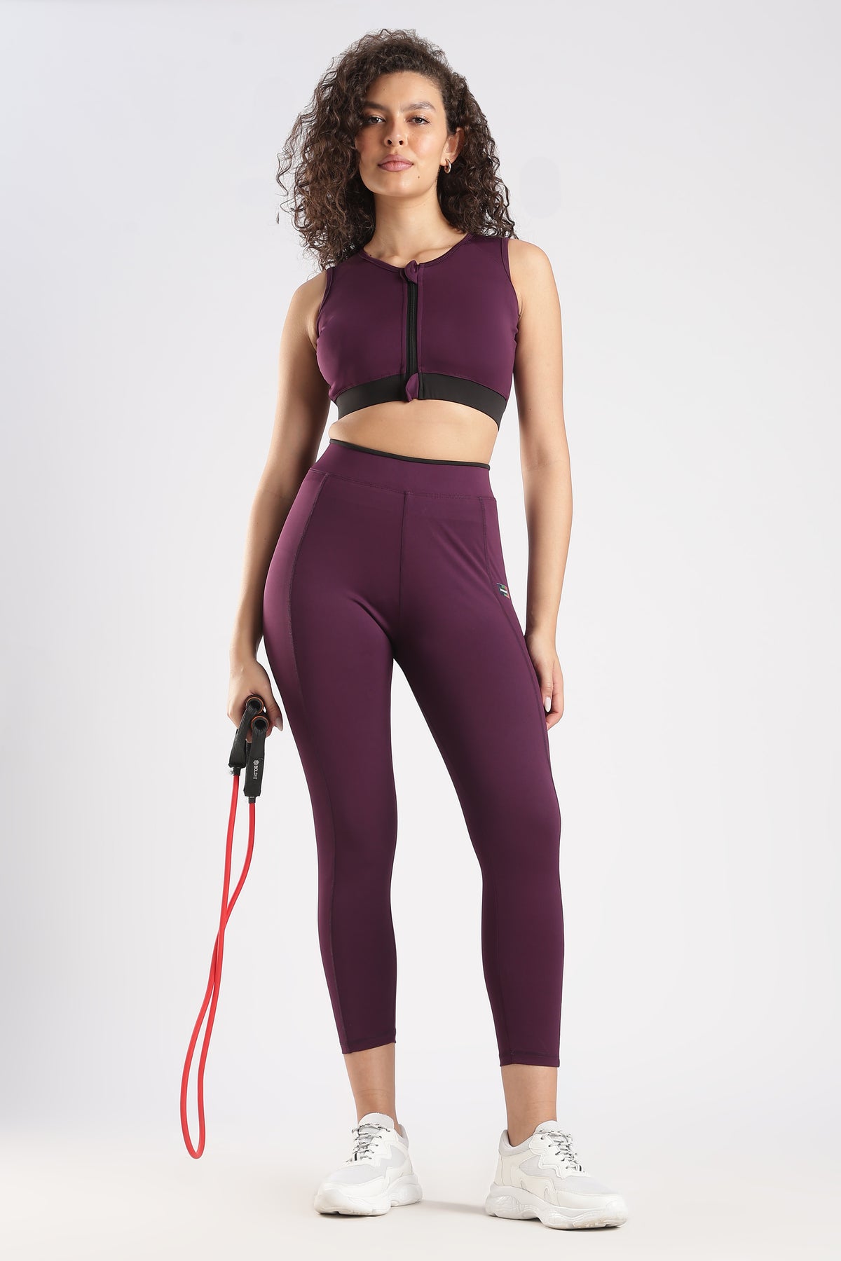 Woman wearing a purple athletic outfit with a sports bra and leggings, holding a resistance band on a white background.