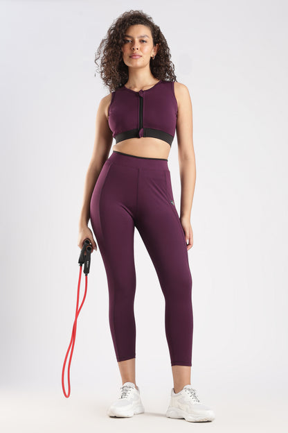 Woman wearing a purple athletic outfit with a sports bra and leggings, holding a resistance band on a white background.