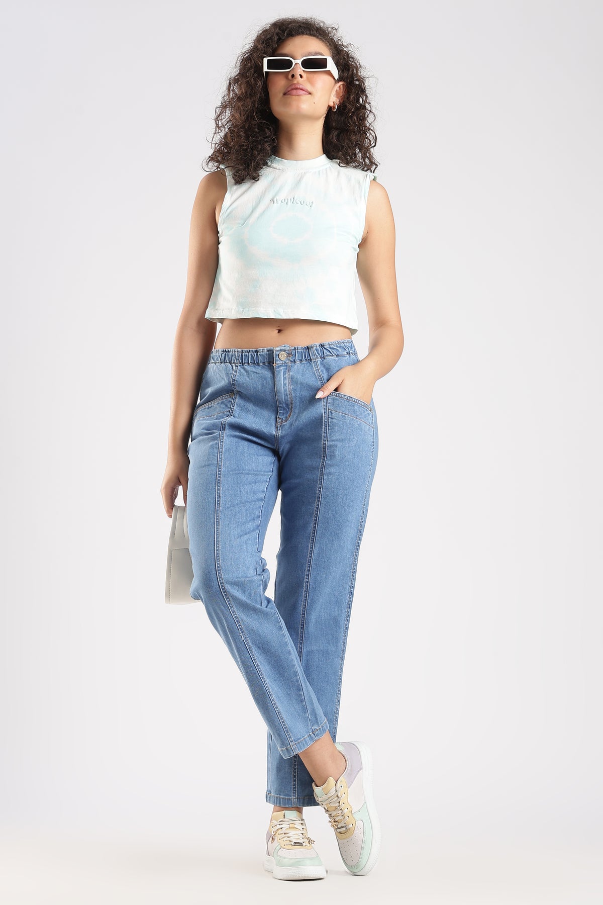 Woman wearing a white sleeveless top and light blue jeans on a white background