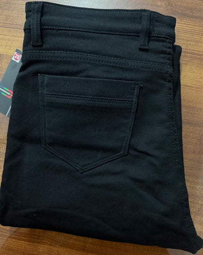 Folded black pants on a wooden surface with a brand tag visible.
