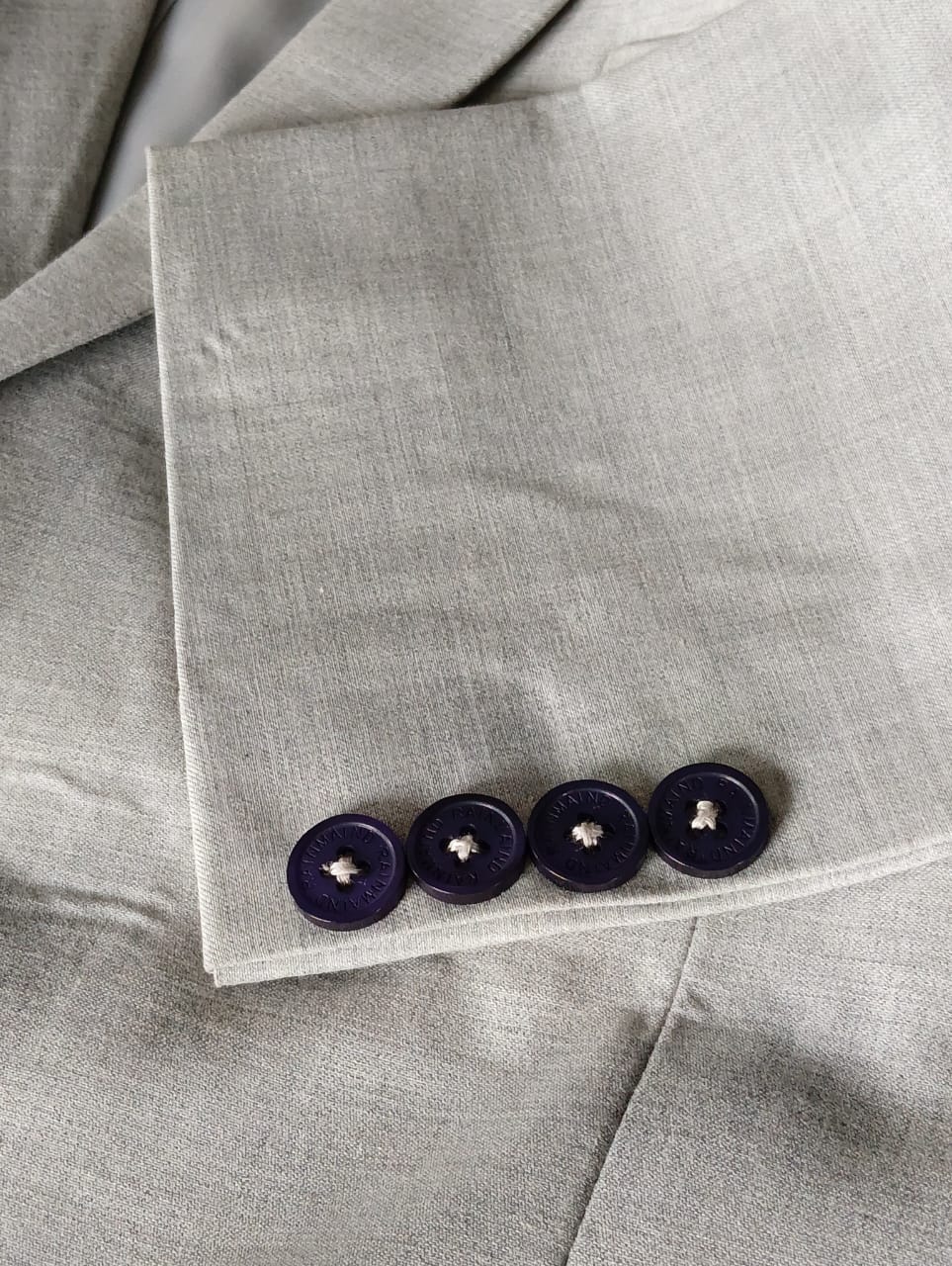 Close-up of a gray fabric with four dark buttons on a matching gray background