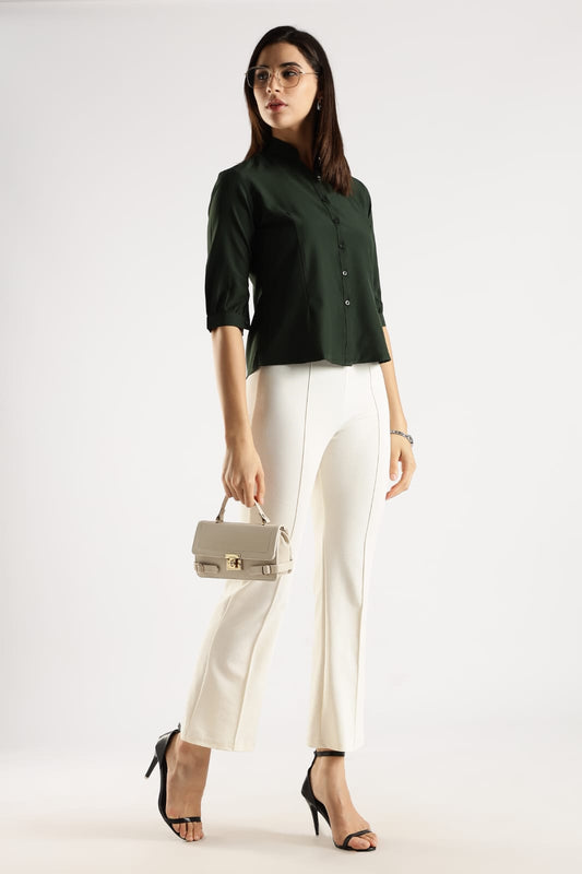 Woman wearing a green shirt and white pants holding a handbag on a white background
