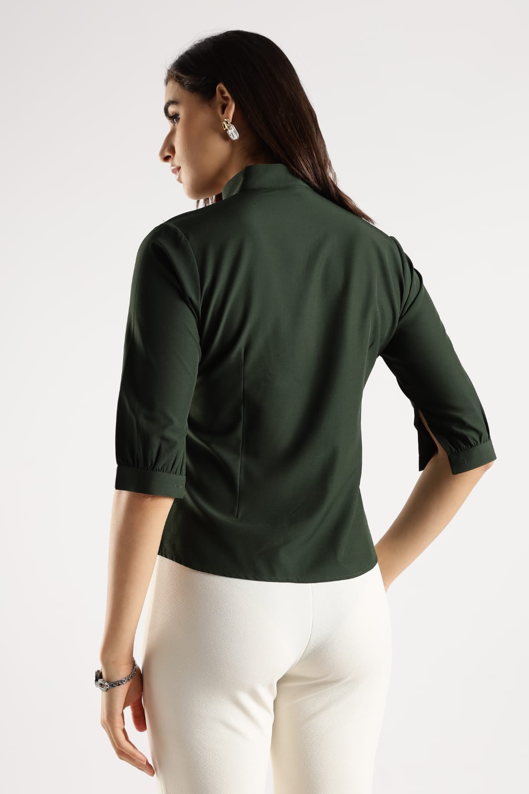 Woman wearing a green blouse with white pants on a light gray background