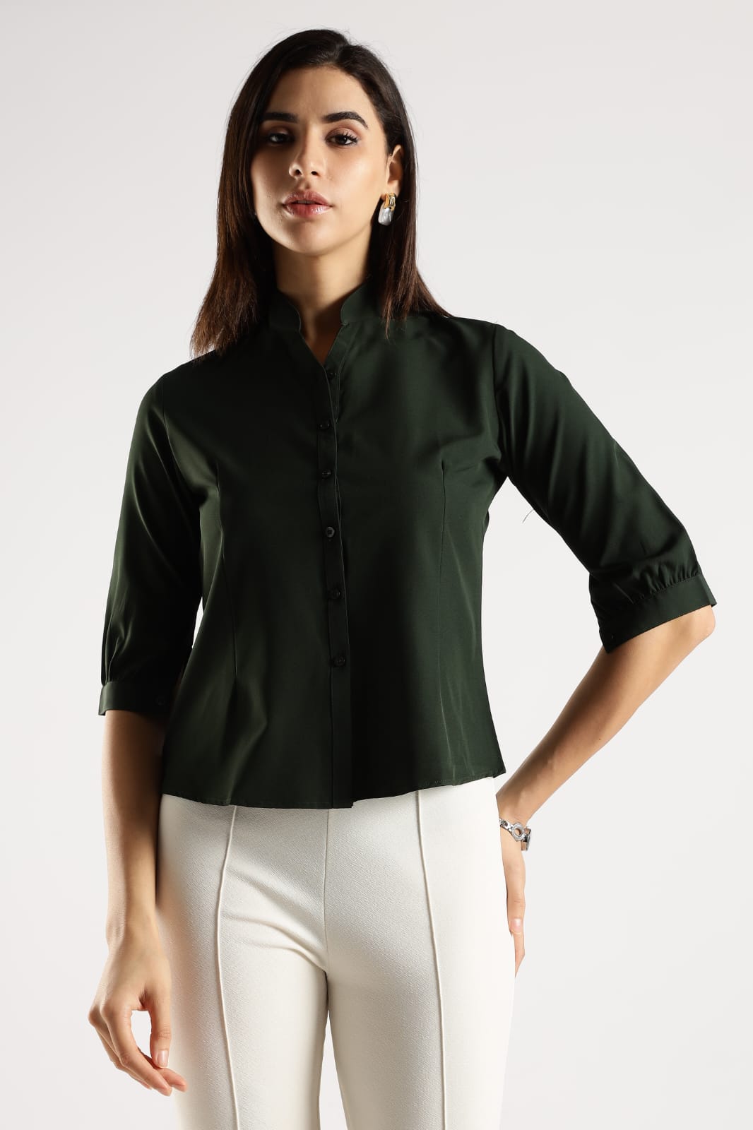 Woman wearing a dark green shirt and white pants on a plain background