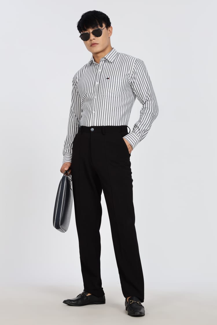 Man in a striped shirt and black pants standing next to a black stool on a white background