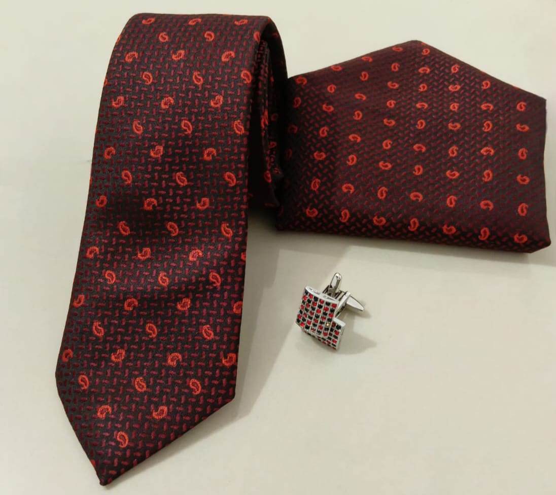 Red patterned tie, matching pocket square, and cufflinks on a light gray background