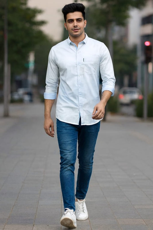 Man walking on a sidewalk wearing a light blue shirt and jeans.