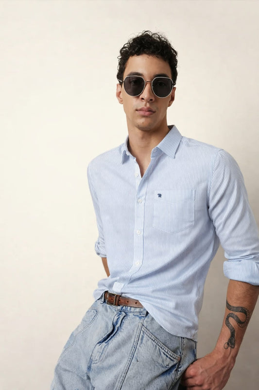 Man wearing a light blue striped shirt and sunglasses against a beige background