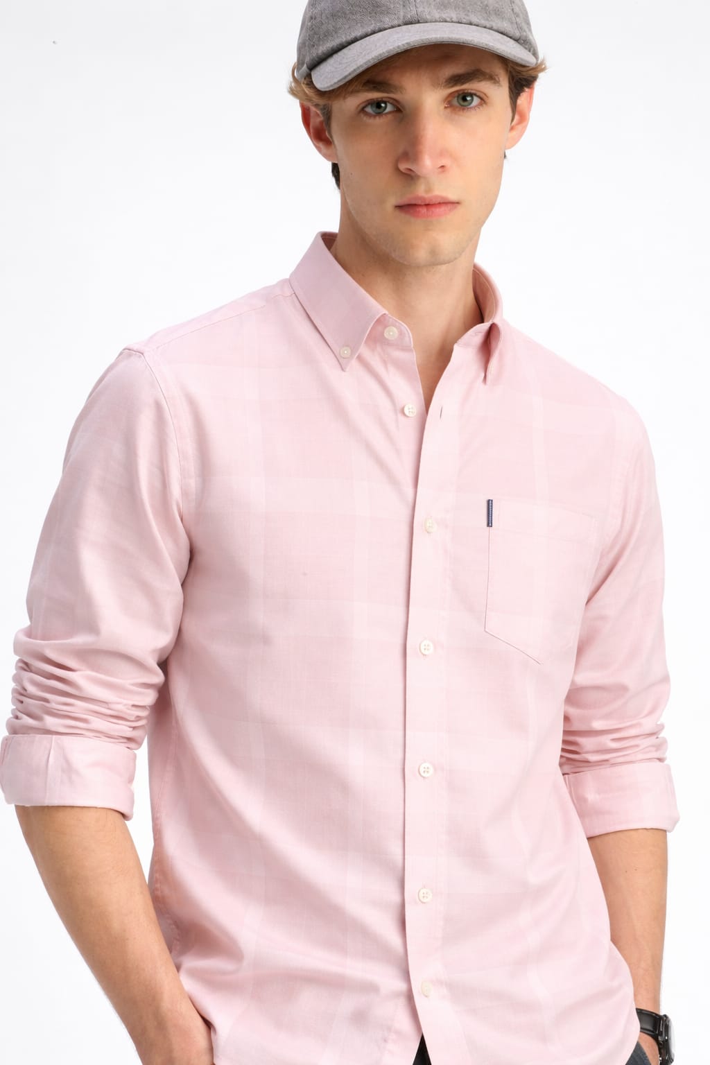 Man wearing a light pink shirt and gray cap on a white background