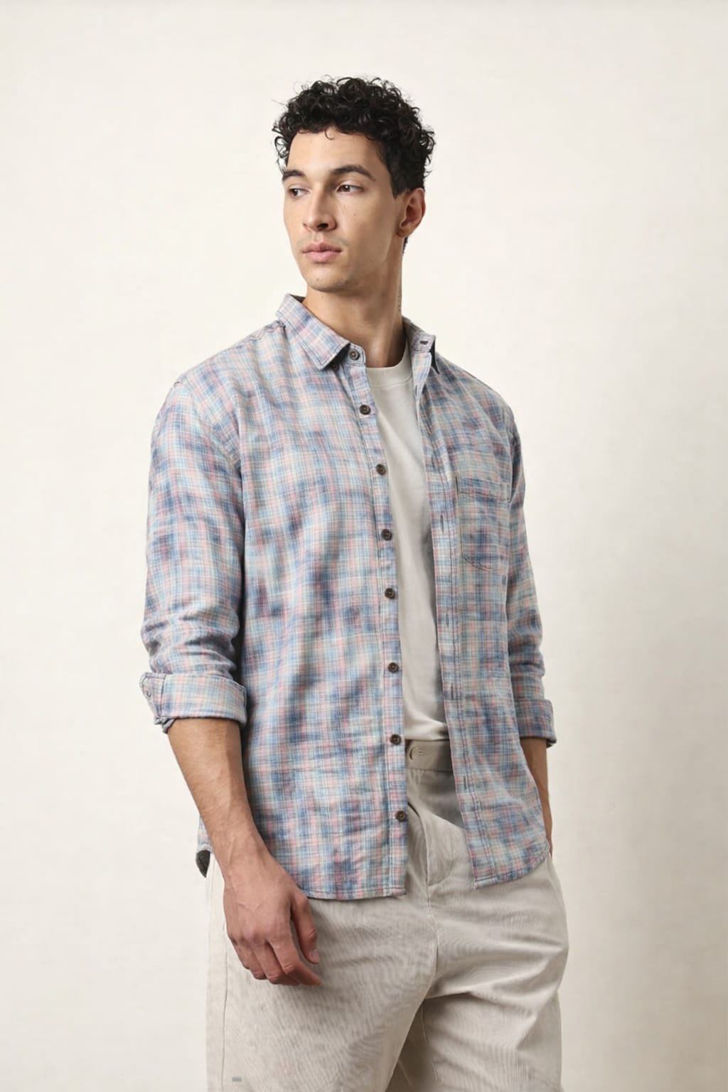 Man wearing a plaid shirt over a white t-shirt with beige pants on a plain background