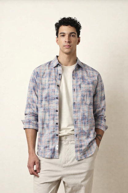Man wearing a plaid shirt over a white t-shirt with beige pants on a plain background