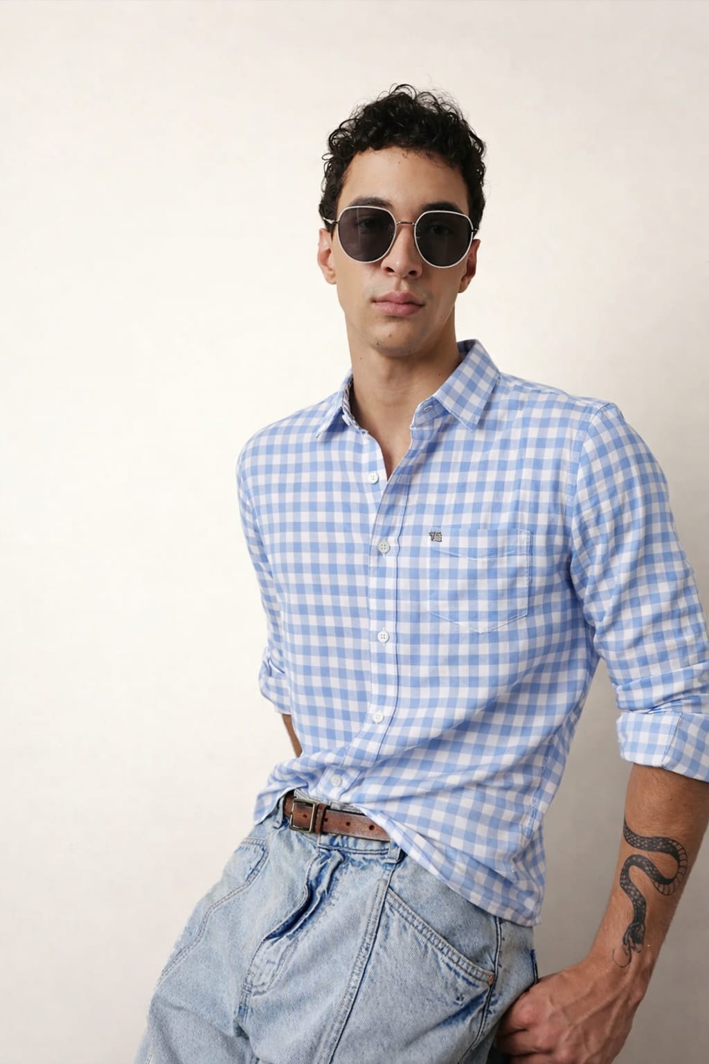 Man wearing a blue checkered shirt and sunglasses against a plain background