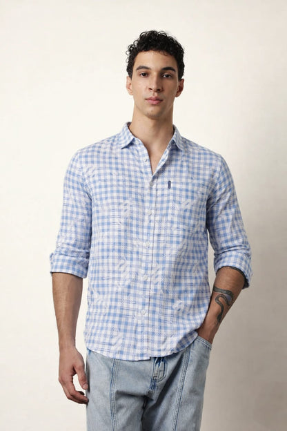 Man wearing a blue checkered shirt and light gray pants against a plain background