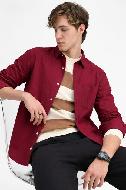 Man wearing a red shirt over a white sweater with black pants on a white background