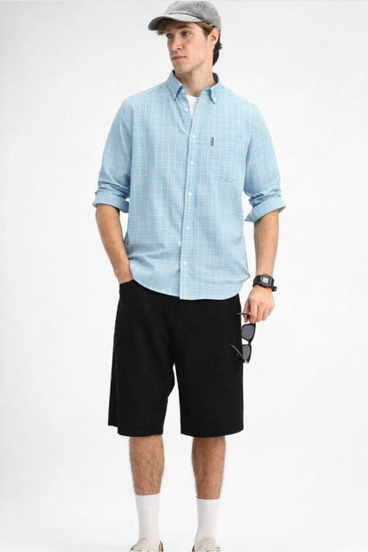 Man wearing a light blue checkered shirt, black shorts, and a cap on a white background