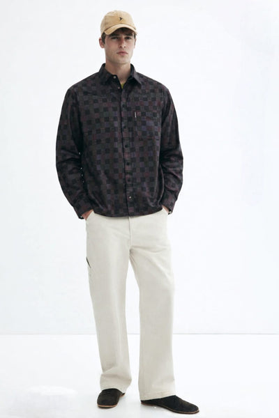 Man wearing a patterned shirt, beige cap, and white pants on a white background