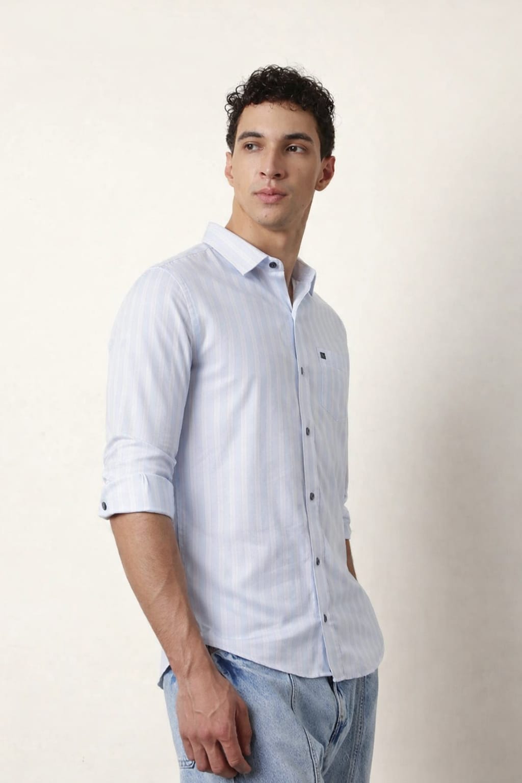 Man wearing a light blue button-up shirt and jeans against a plain background