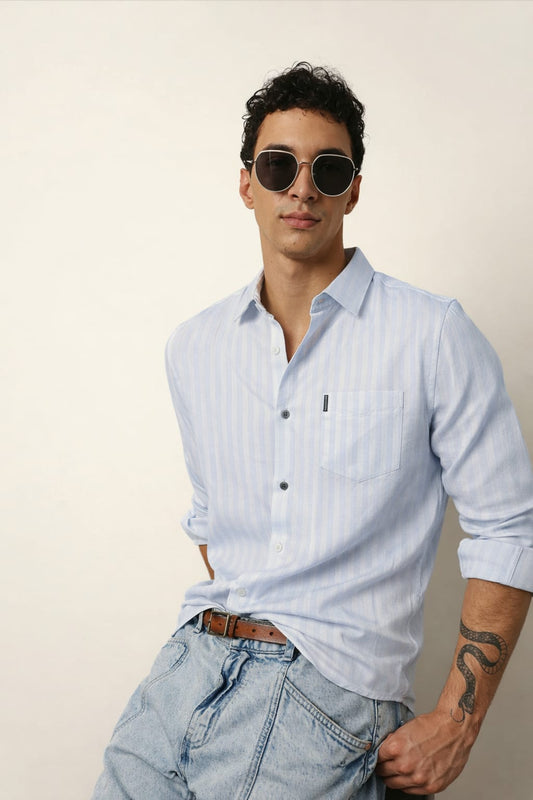 Man wearing a light blue striped shirt and sunglasses against a plain background