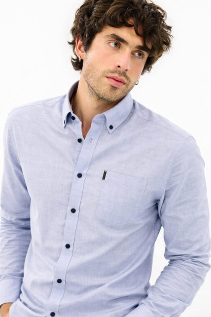 Man wearing a light blue button-up shirt with black buttons on a white background