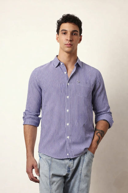 Man wearing a purple striped shirt and light blue jeans against a plain background