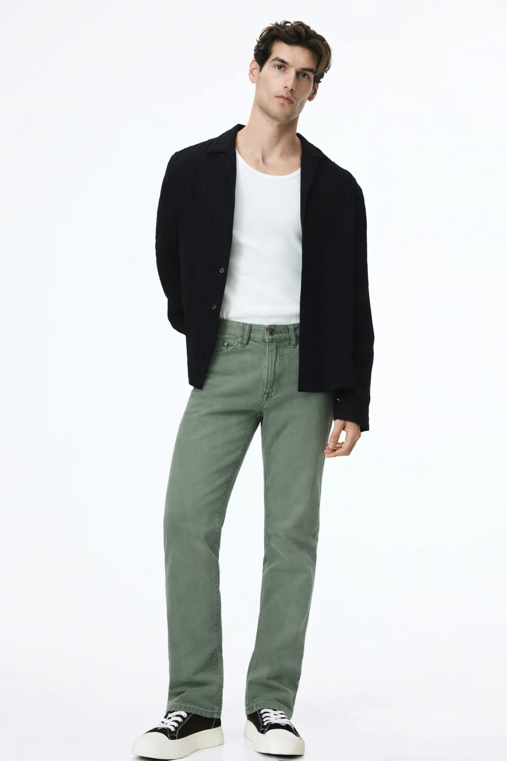 Man wearing a black jacket, white shirt, green pants, and black shoes on a white background