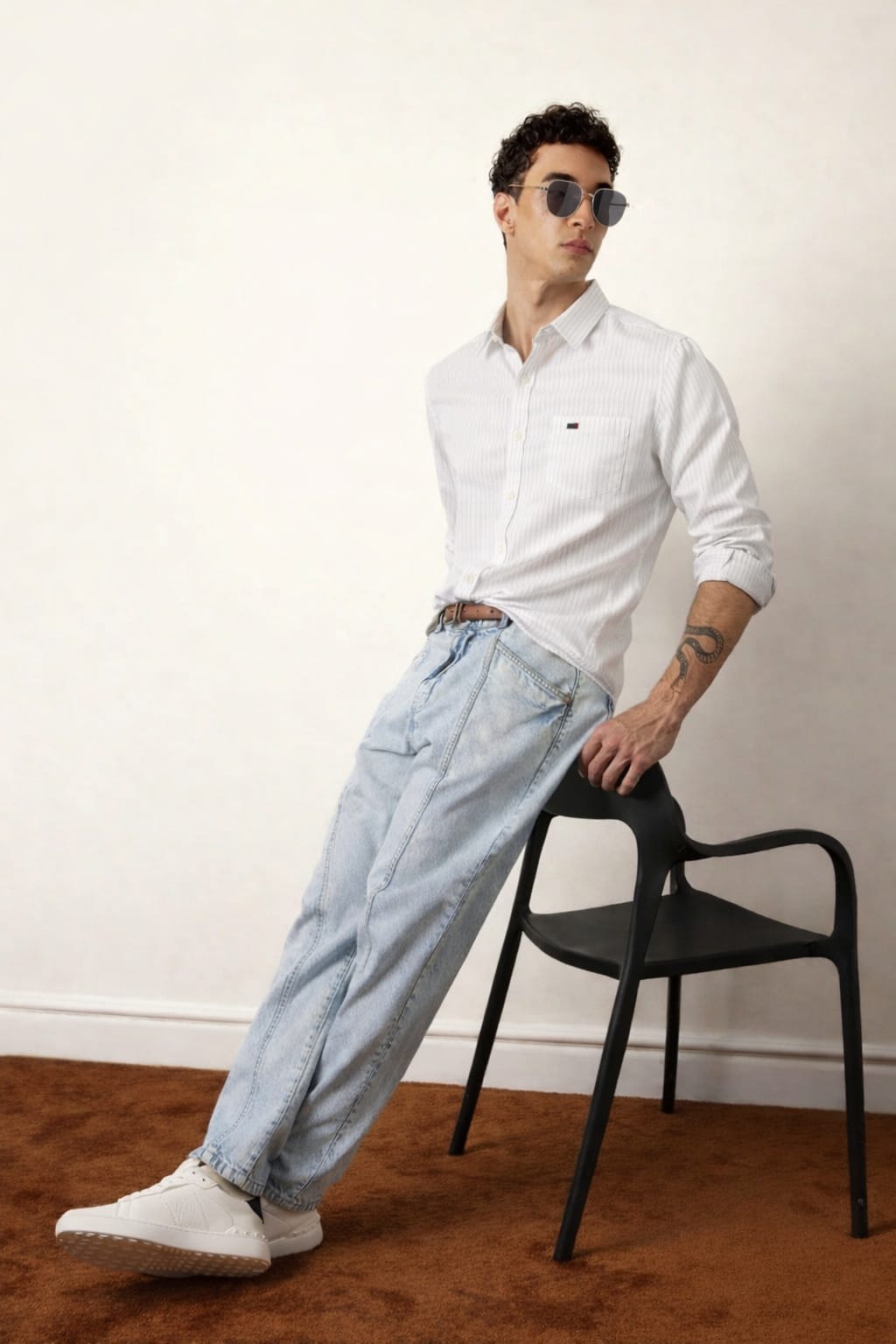 Man wearing a white shirt and light blue jeans leaning against a black chair.