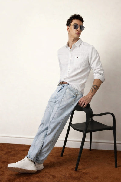Man wearing a white shirt and light blue jeans leaning against a black chair.
