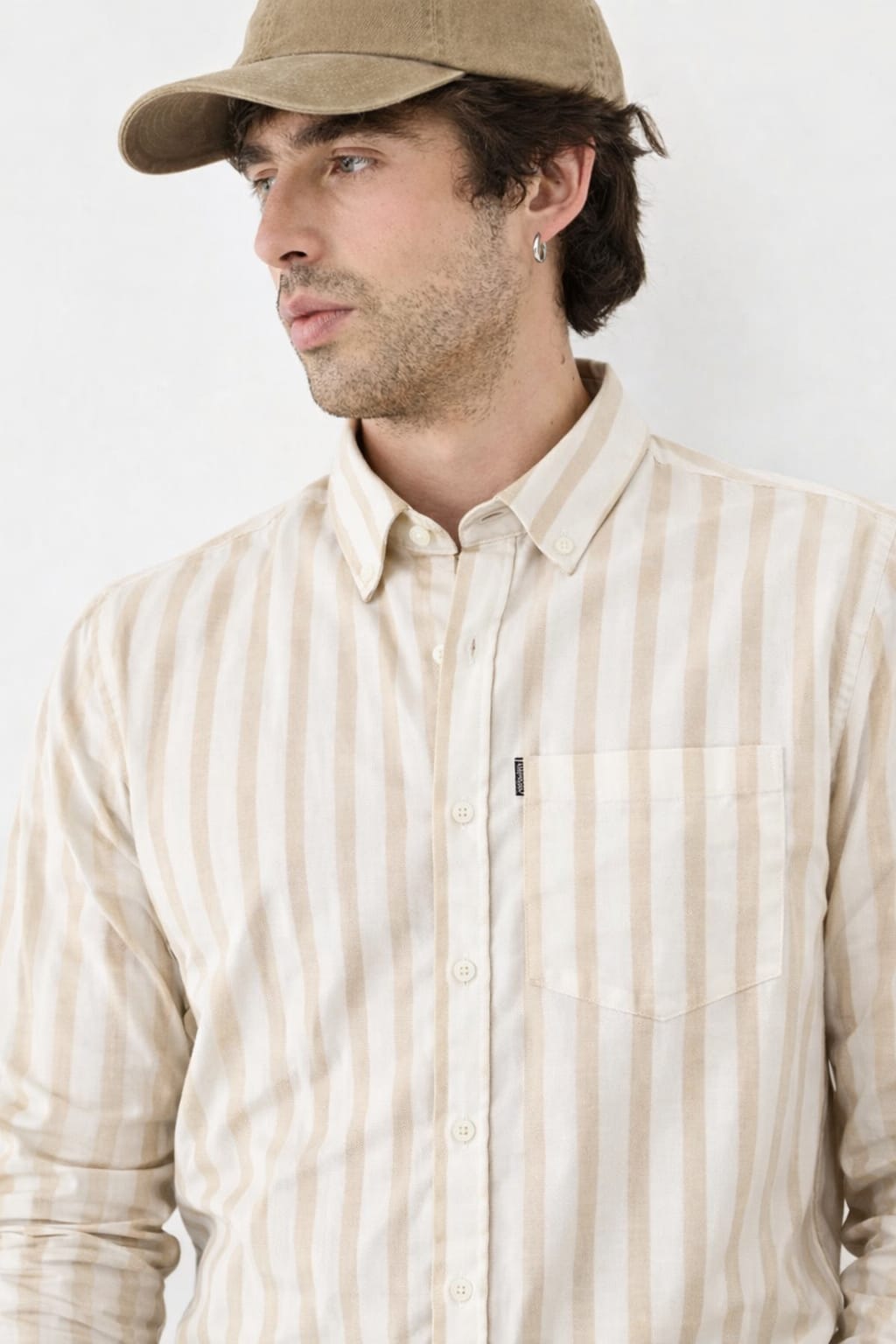 Man wearing a beige striped shirt and cap against a white background