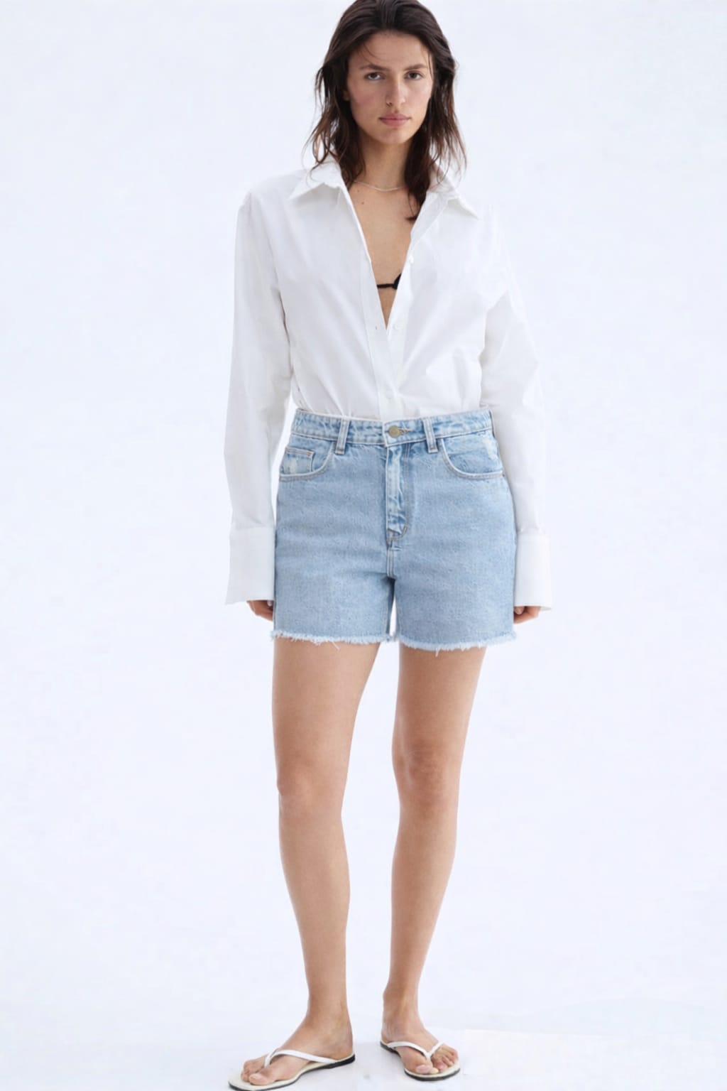 Woman wearing a white blouse and light blue denim shorts on a white background