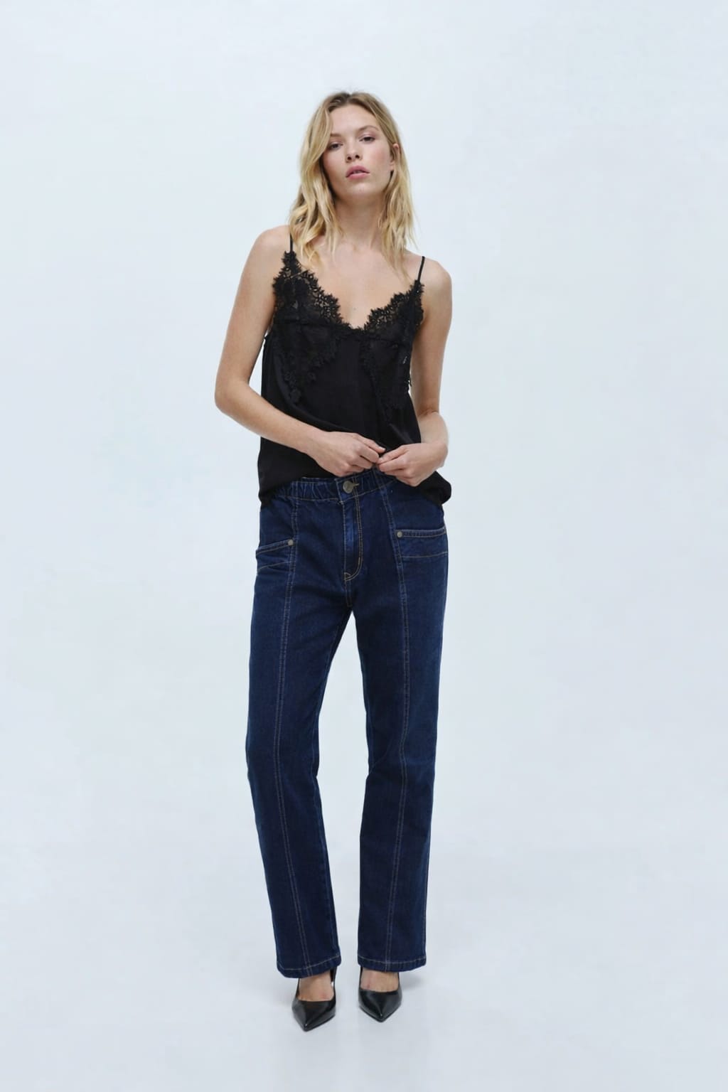 Woman wearing a black lace top and dark blue jeans on a white background
