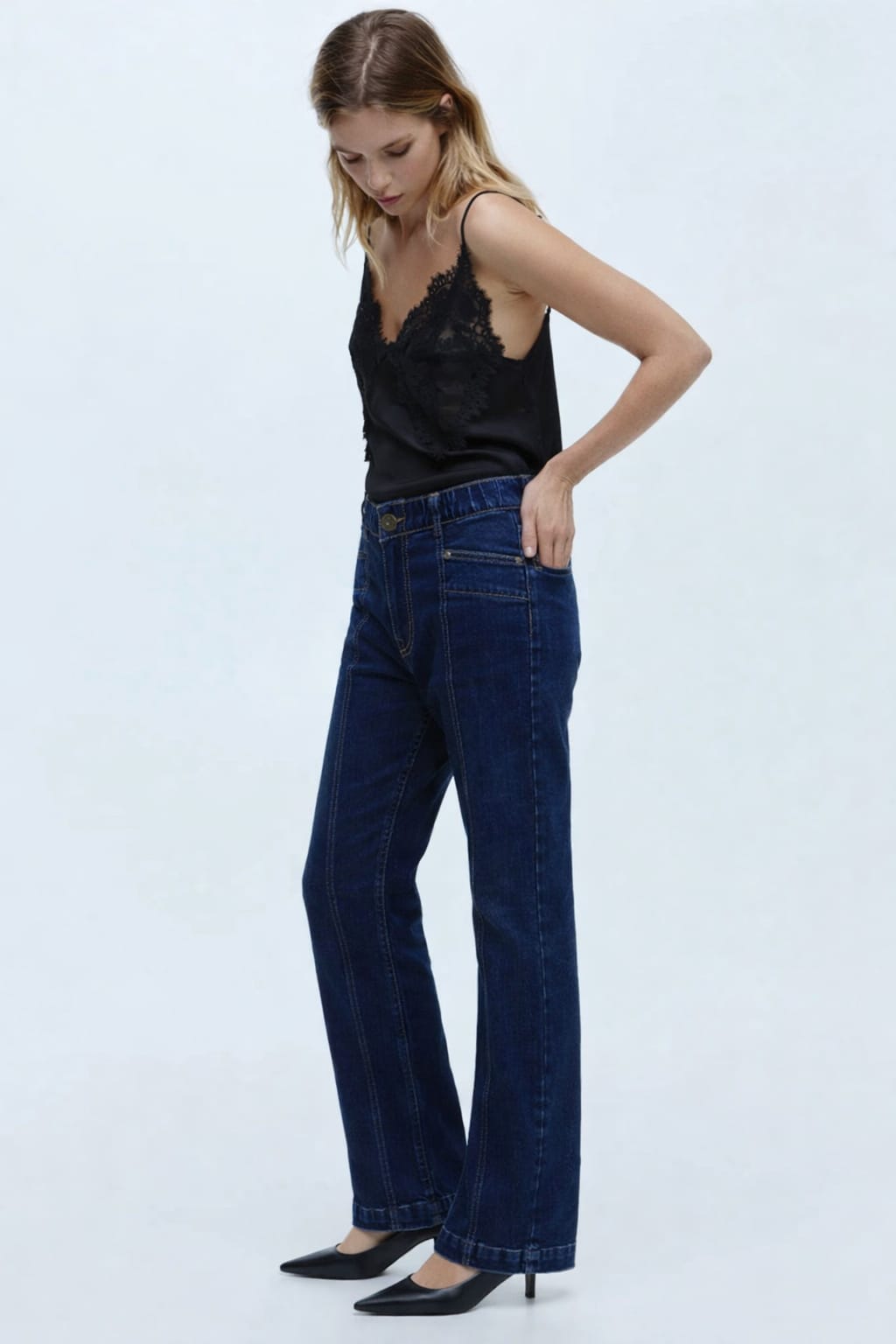 Woman wearing dark blue jeans and a black top on a light gray background