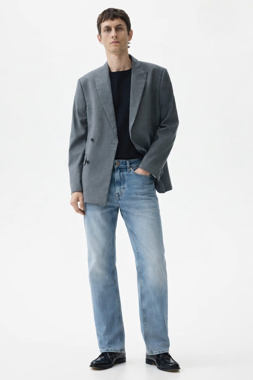 Man wearing a gray blazer, black shirt, and light blue jeans on a white background