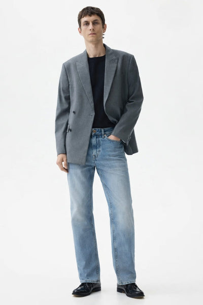 Man wearing a gray blazer, black shirt, and light blue jeans on a white background