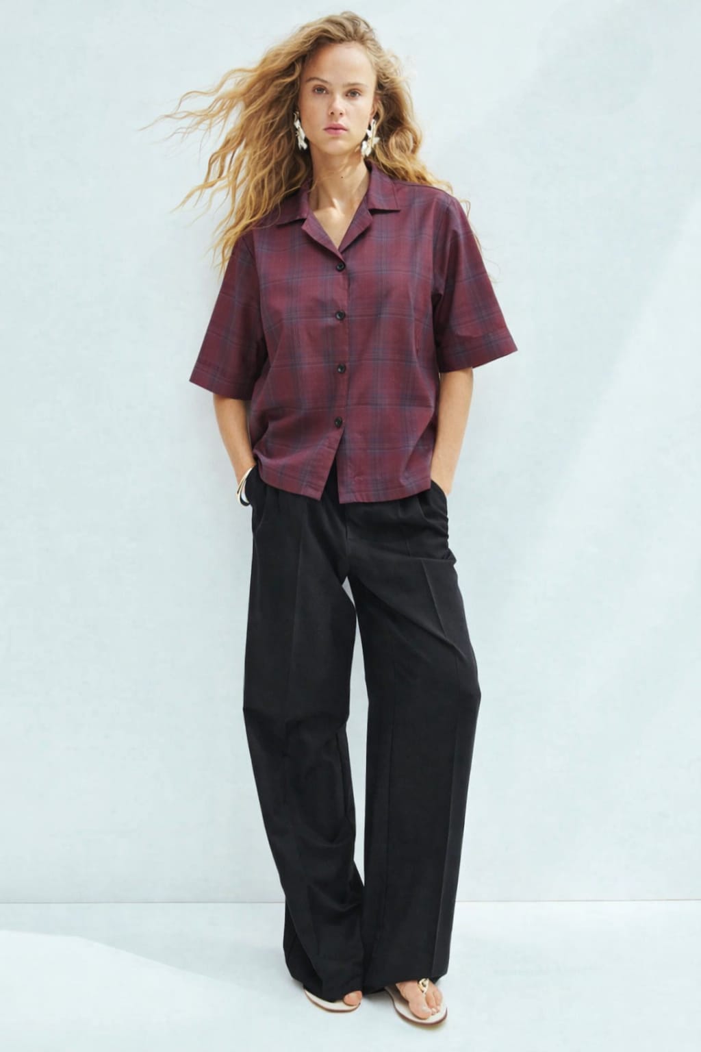 Woman wearing a plaid shirt and black pants against a light blue background