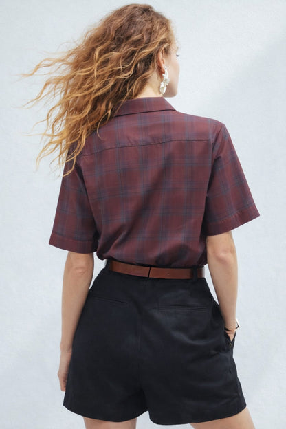 Person wearing a plaid shirt and black shorts against a plain background