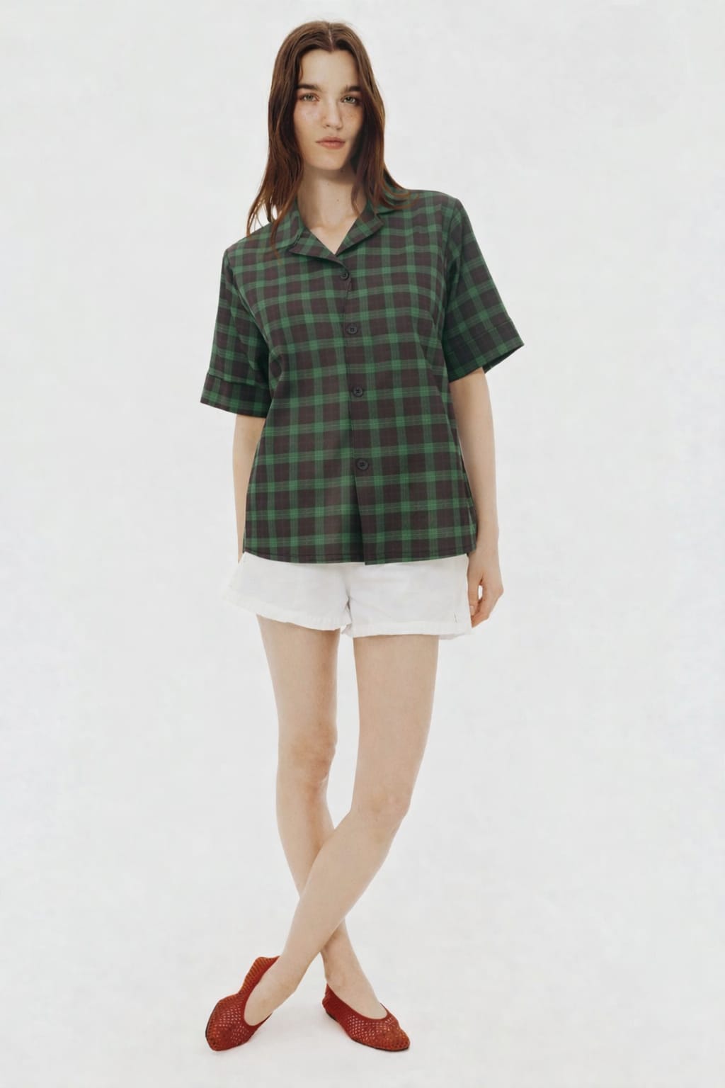 Woman wearing a green plaid shirt and white shorts on a white background