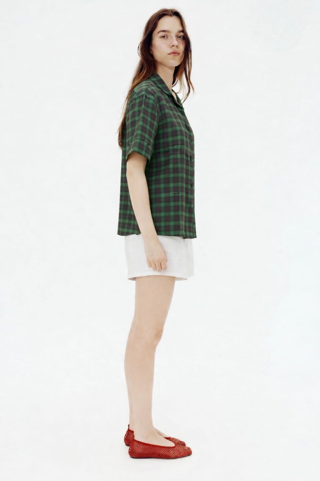 Woman wearing a green plaid shirt and white shorts on a white background