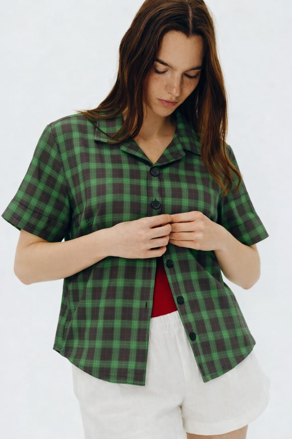 Woman wearing a green plaid shirt and white shorts on a white background