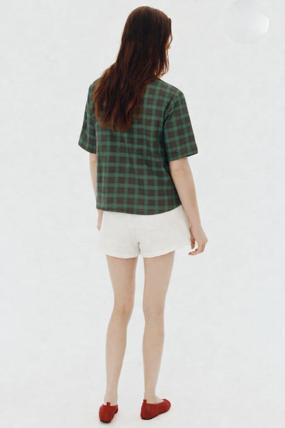 Person wearing a green plaid shirt and white shorts on a white background