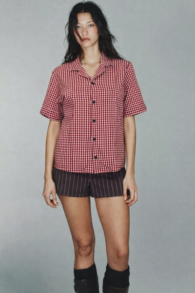 Person wearing a red and white checkered shirt with black shorts on a gray background