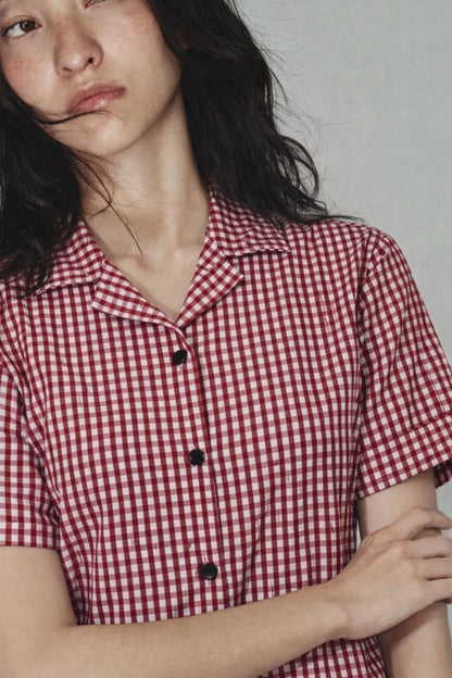 Person wearing a red and white checkered shirt with black buttons against a plain background